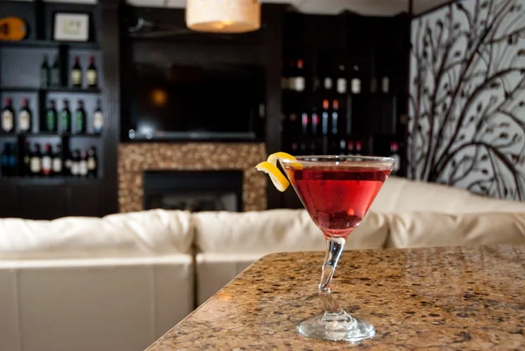 A cocktail on the bar, with the lounge, wine shelves and tree mural behind it